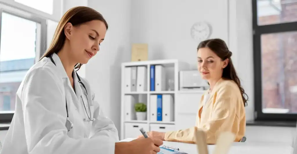 Doctor taking notes while meeting with a female patient in a clinic office