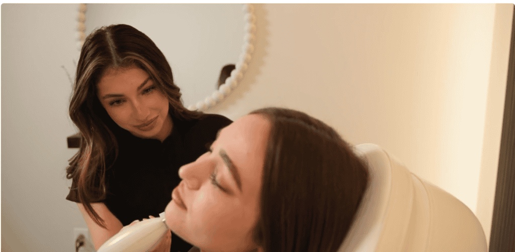 Aesthetician preparing a client’s face as she reclines in a treatment chair