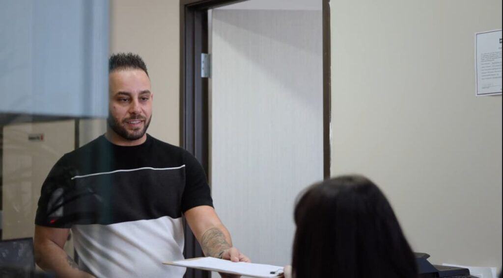 Man talking with a staff member across the table in a clinic consultation room