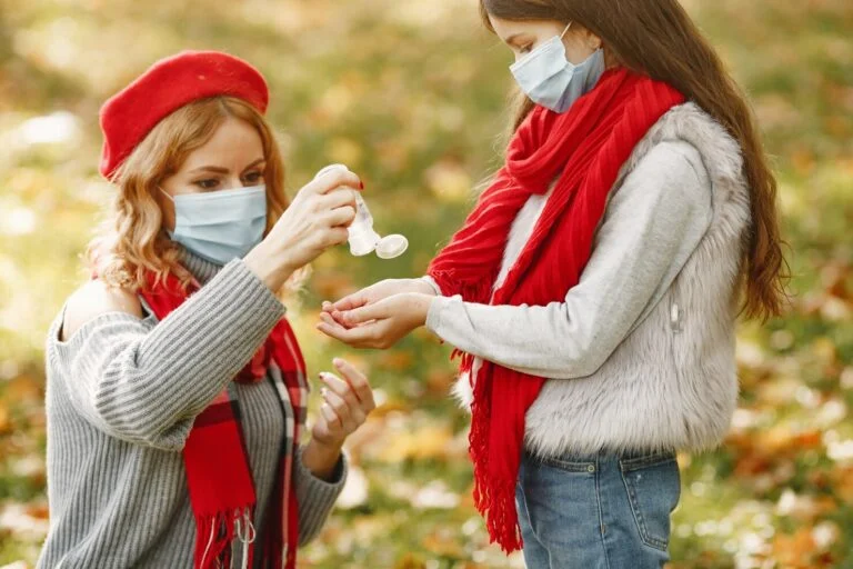 Mother and daughter in face masks using hand sanitizer outdoors