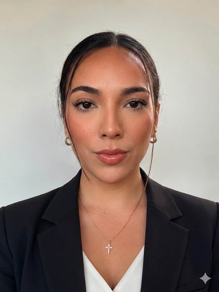 Lucy in a black blazer and white top with hair pulled back, light background
